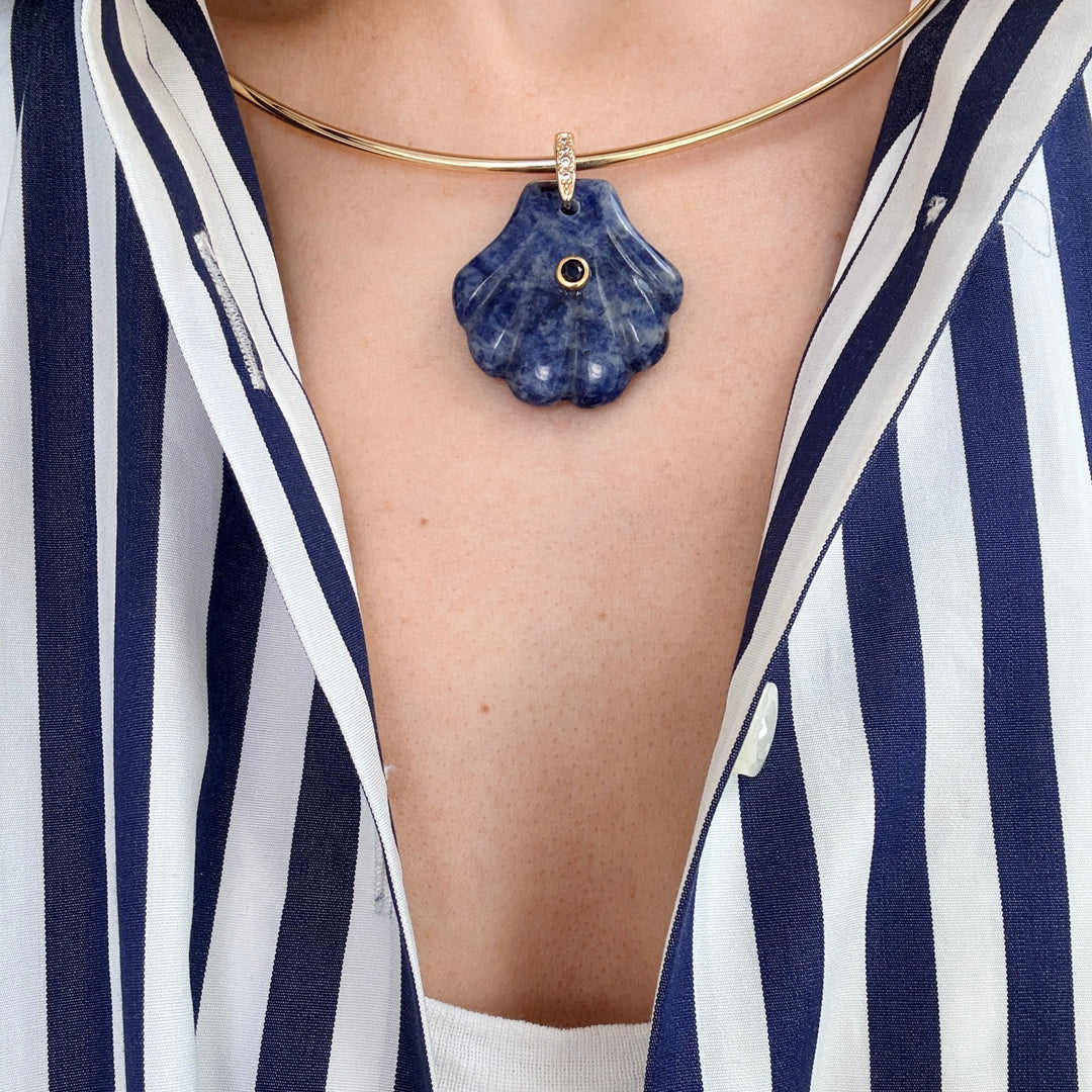 Person wearing a blue stone pendant on a gold chain around their neck, with a striped shirt.